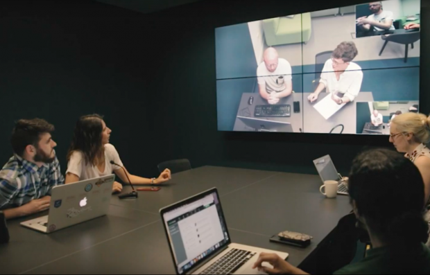 People sitting around a table observing a user research session on a screen