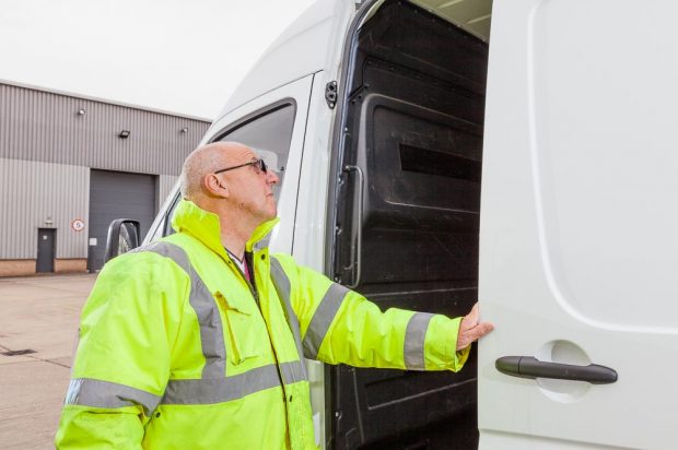 A man wearing a bright fluorescent yellow jacket inspecting the inside of a large white van.