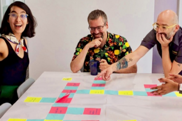 Three members of the Canadian Digital Service, laughing and smiling, around a table on which there is a large assortment of post it notes. 