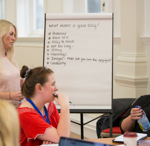 People in a room discussing what makes a good blog post, with points such as ‘easy to read’ written on a board behind them