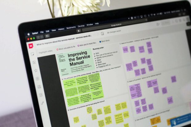 A laptop showing a remote workshop’s collaboration board on improving the Service Manual with dozens of virtual sticky notes on it