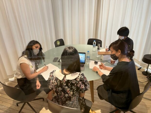 A photograph of a user research session where the researcher is interviewing a Thai participant, the translator is listening to the response and a note taker is taking notes.