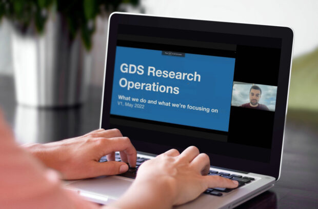 Person typing on a laptop. The laptop screen has a video call with a presentation titled GDS Research Operations.