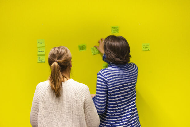 Two people putting post it notes on a wall during training